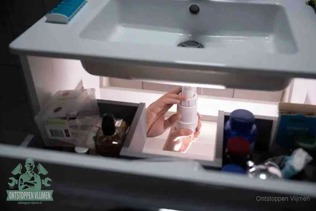 Een pompfles met zeep boven een wastafel, de heet water en afwasmiddel-methode om een vetprop in de afvoer los te maken in Vlijmen