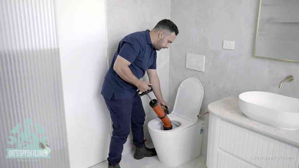 Een monteur buigt over een wandcloset en duwt met de hand een persluchtontstopper in de toiletpot om de verstopping handmatig los te maken in Vlijmen