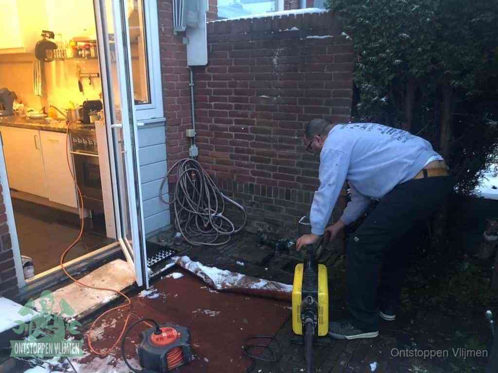 Een monteur werkt buiten bij een open riool-/grondput met een elektrische ontstoppingsmachine om een verborgen afvoerprobleem op te sporen in Vlijmen