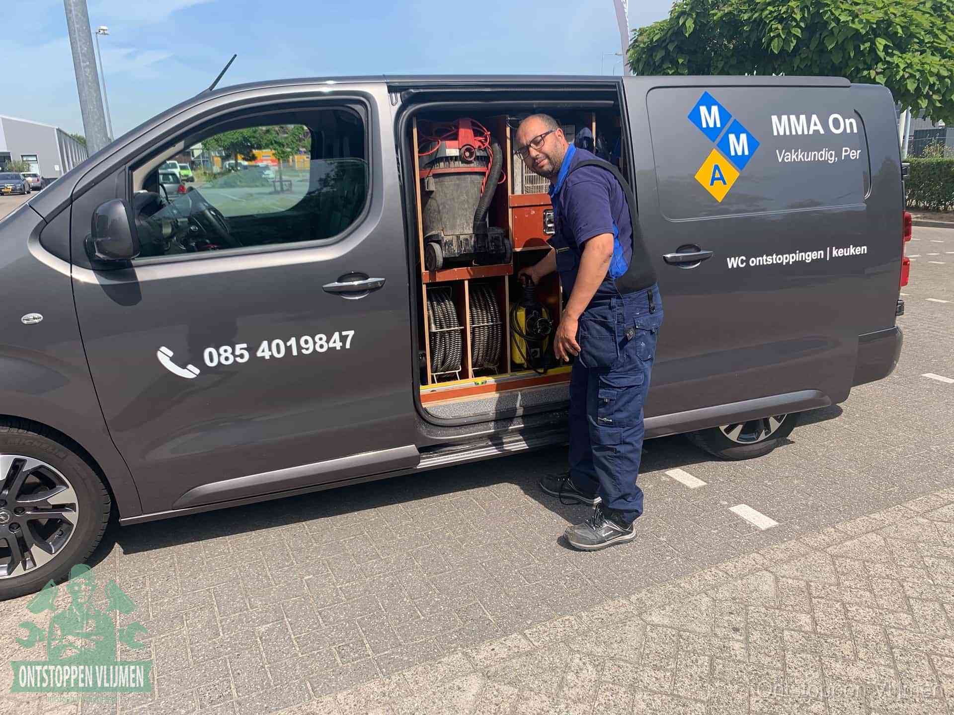 Een monteur bij de open schuifdeur van zijn bedrijfsbus op een parkeerplaats, klaar om de oorzaak van terugkerende afvoerverstoppingen aan te pakken in Vlijmen
