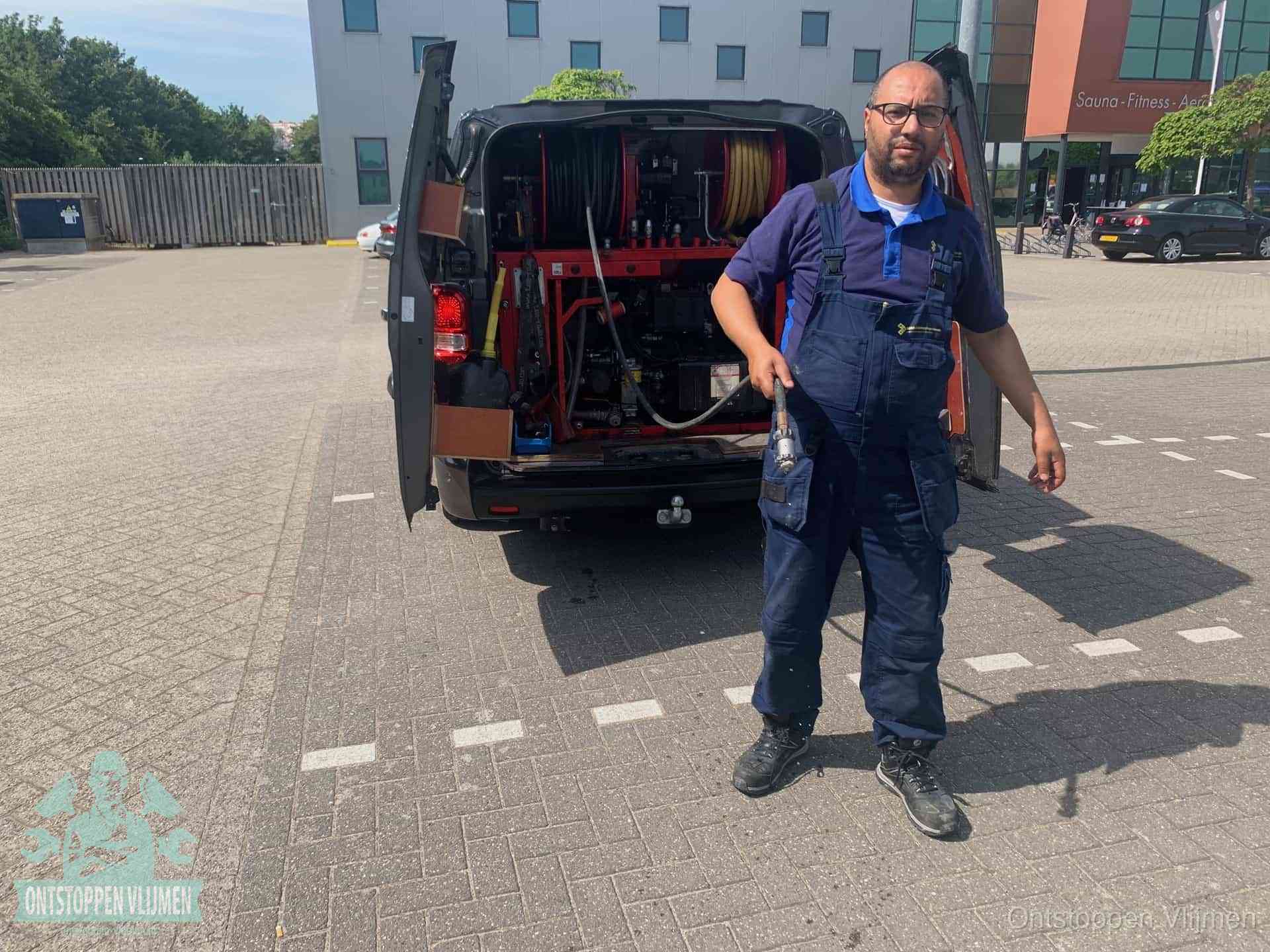 Een monteur bij zijn bestelbus met een hogedruk- en rioolreinigingsunit, klaar om de oorzaak van terugkerende wc-verstoppingen aan te pakken in Vlijmen