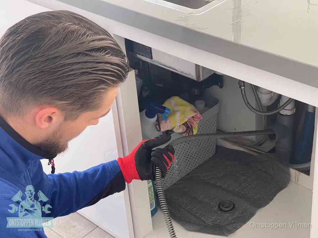 Een monteur voert een flexibele ontstoppingsveer in de afvoer om een verstopping voorbij de bocht van het toilet te bereiken in Vlijmen