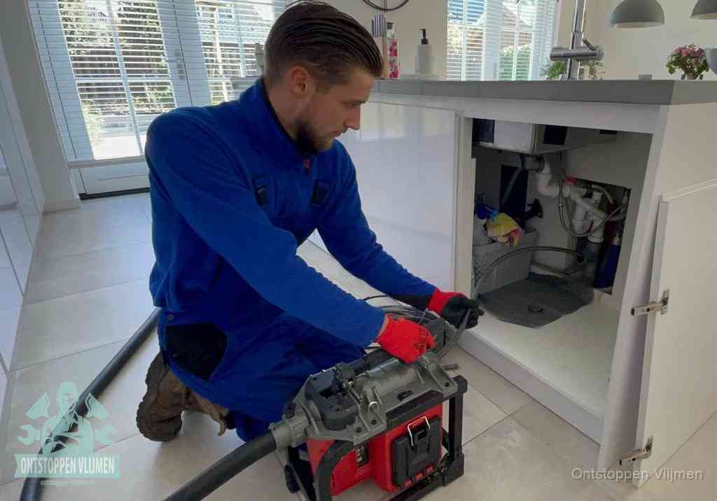 Een monteur voert een professionele elektrische ontstoppingsmachine in de afvoer onder de spoelbak tijdens het gootsteen ontstoppen in Vlijmen